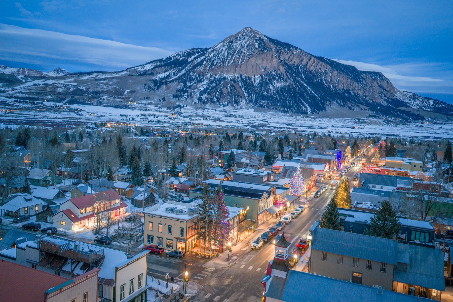 Town lit up for the holidays, snowy mountain in background.