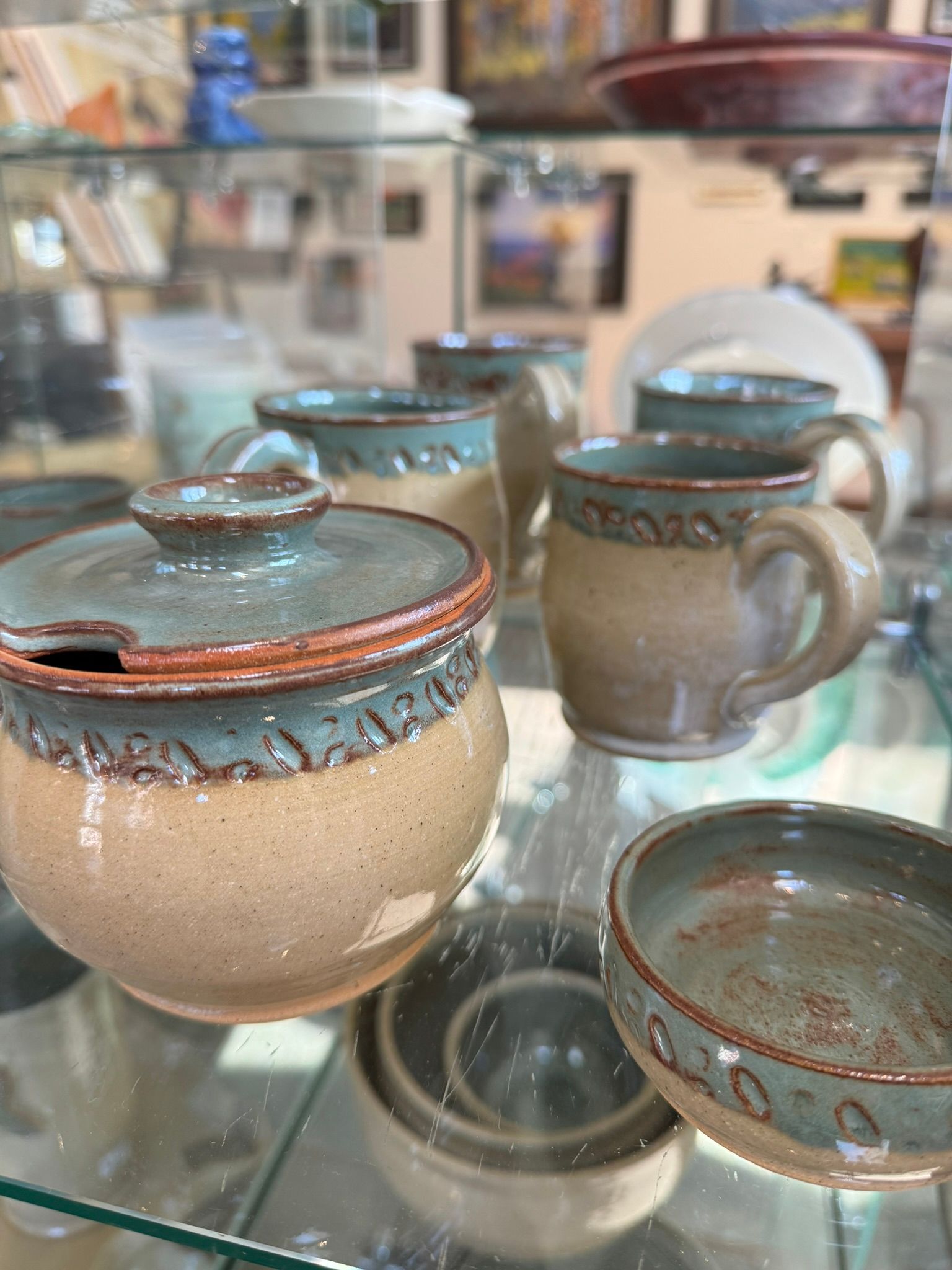 A group of ceramic cups and bowls are sitting on a glass shelf.