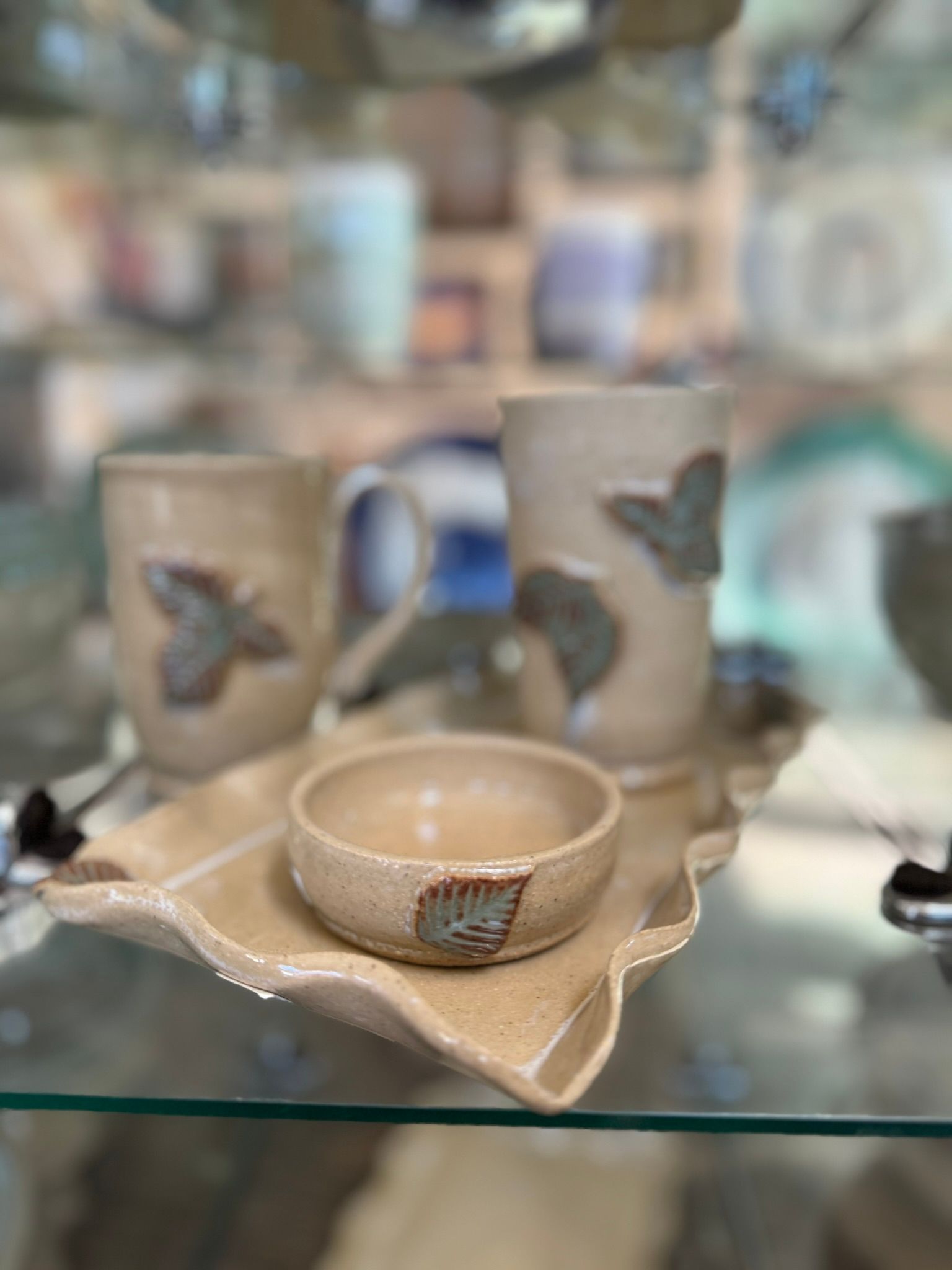 A tray with two cups and a bowl on it is on a glass shelf.