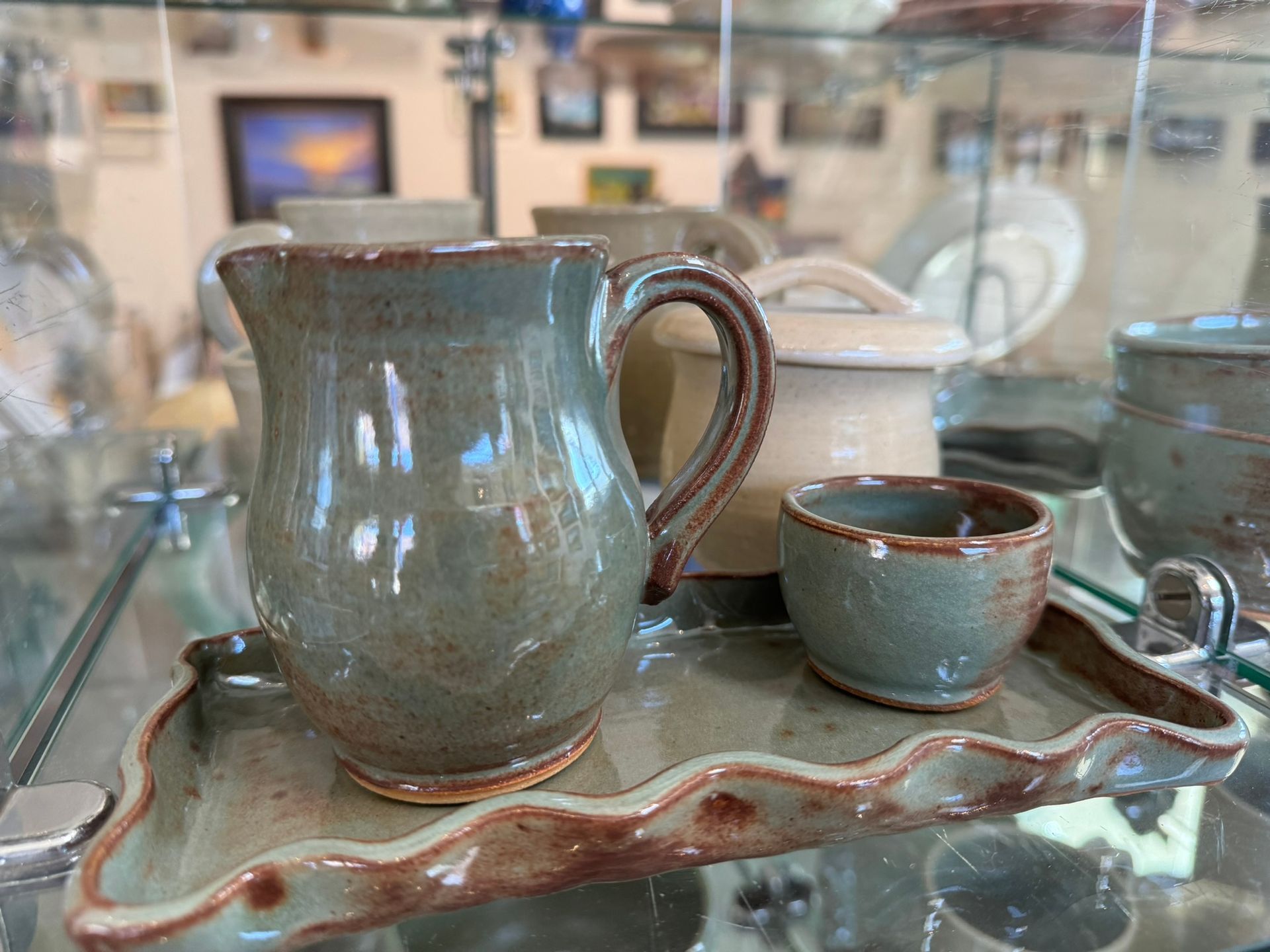A pitcher , cup , and tray are on display in a glass case.