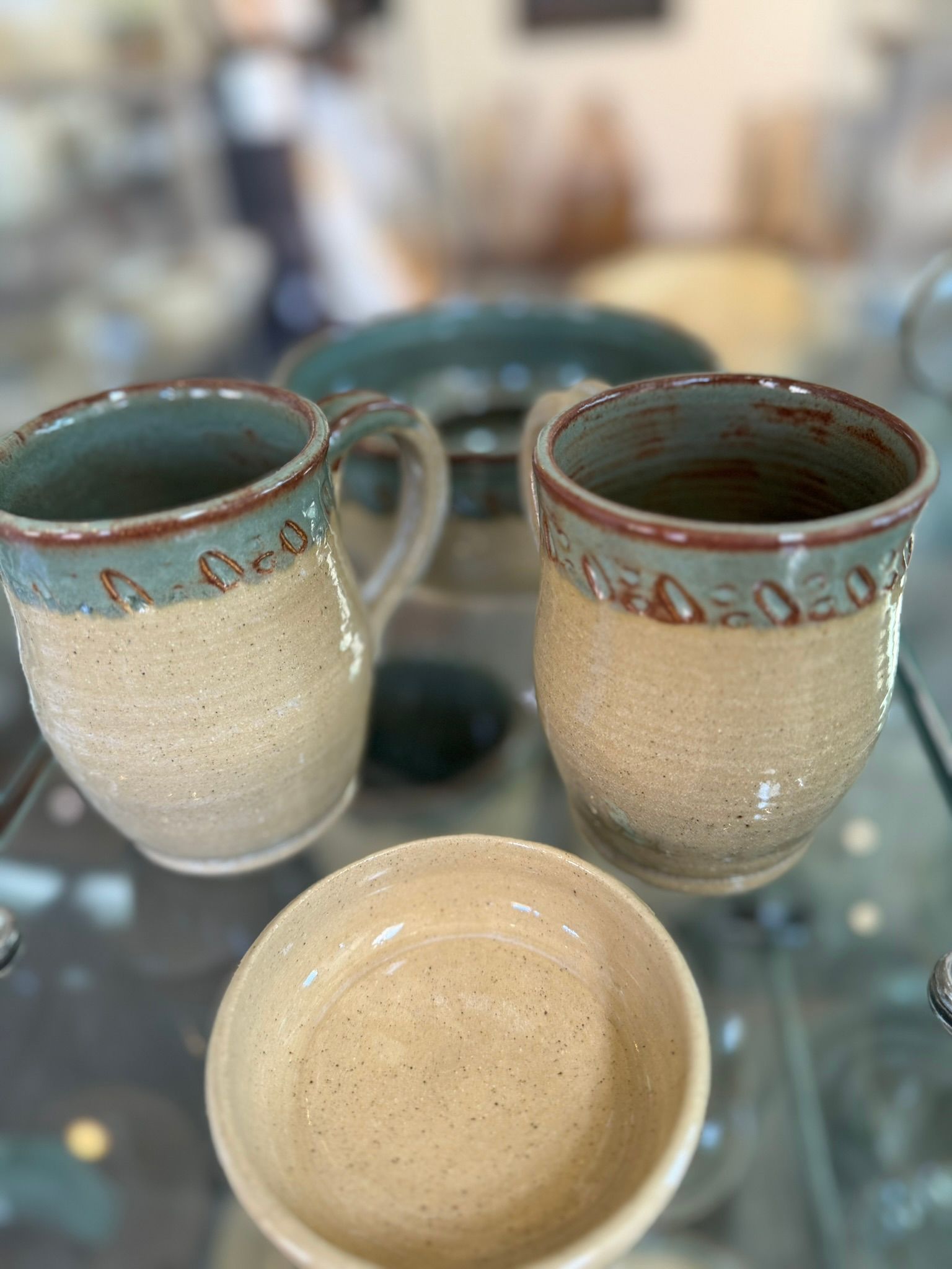 Two mugs and a bowl are sitting on a glass table.