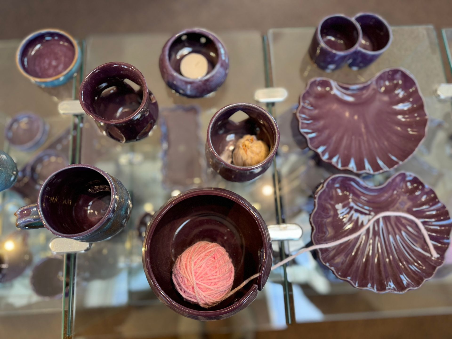 A table topped with purple ceramics and a ball of yarn.
