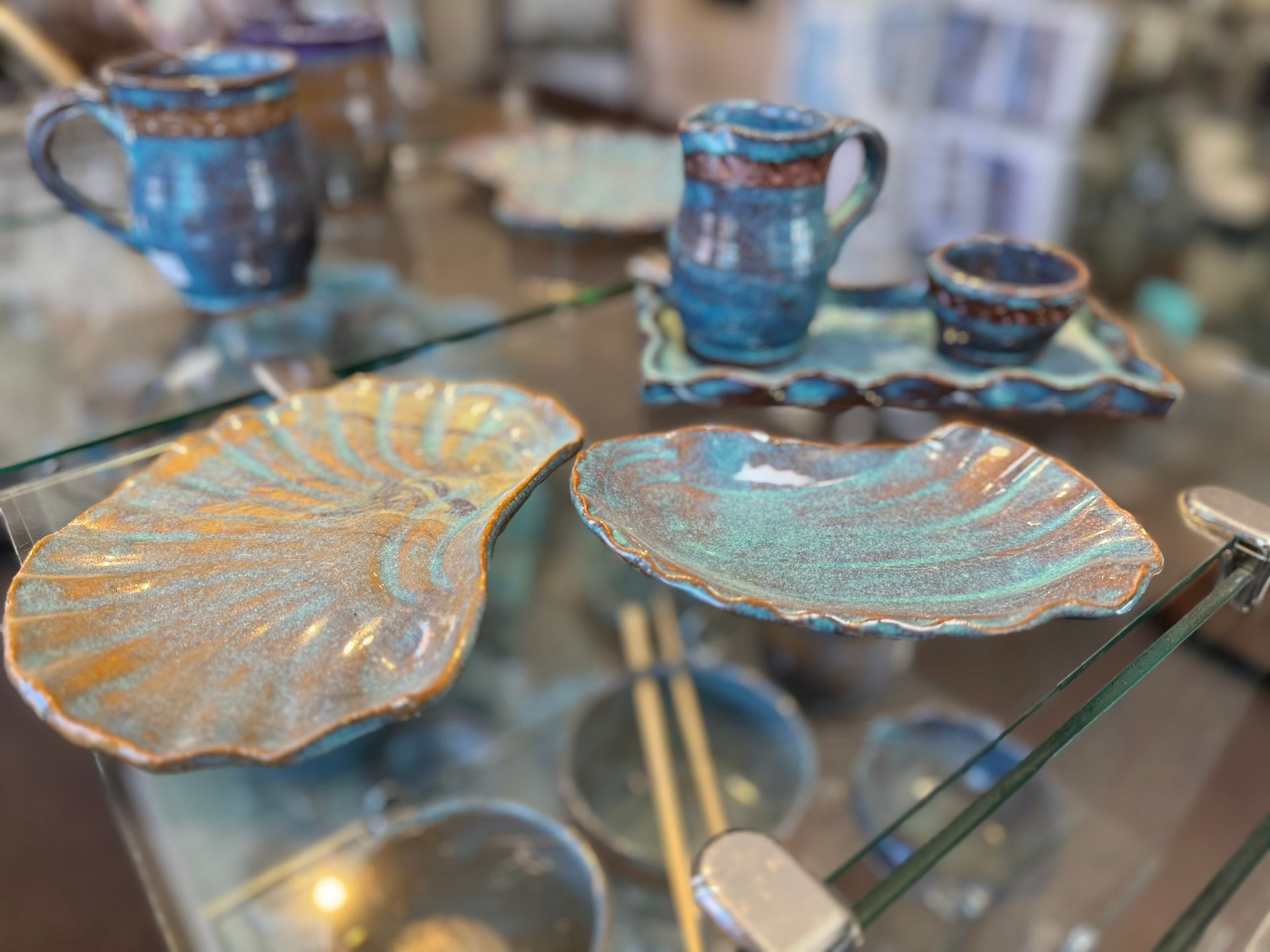 A glass table topped with plates , cups , and chopsticks.