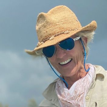 A woman wearing a straw hat and sunglasses is smiling.