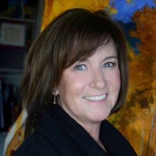 A woman in a black jacket is smiling in front of a painting.