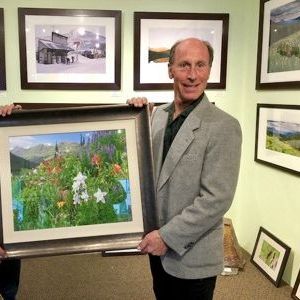 A man in a suit is holding a framed painting of flowers.