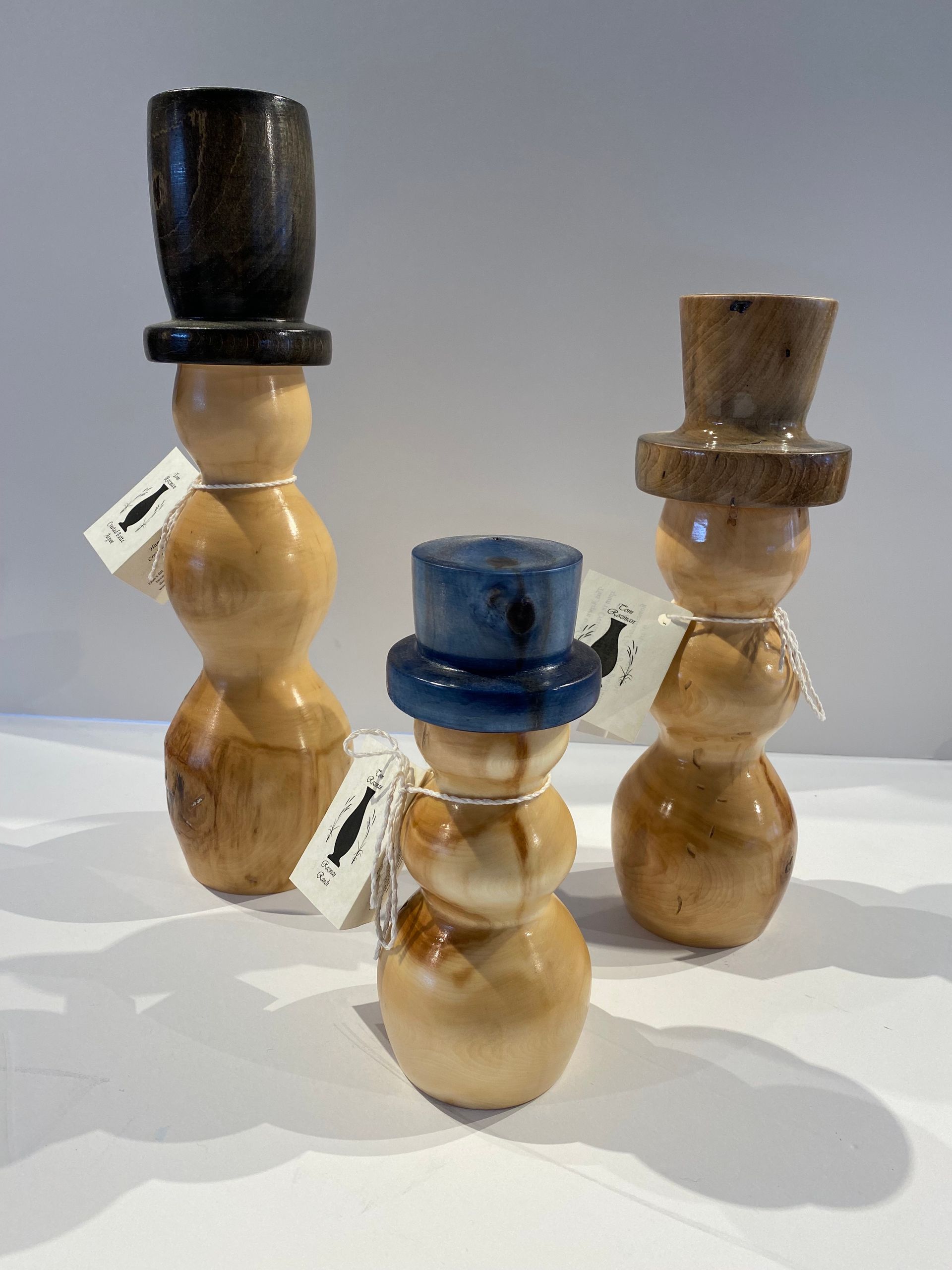 Three wooden snowmen with hats are sitting on a table.