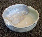 A white bowl with a handle is sitting on a carpet.