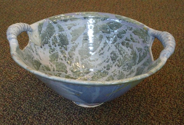 A large bowl with handles is sitting on a brown carpet.