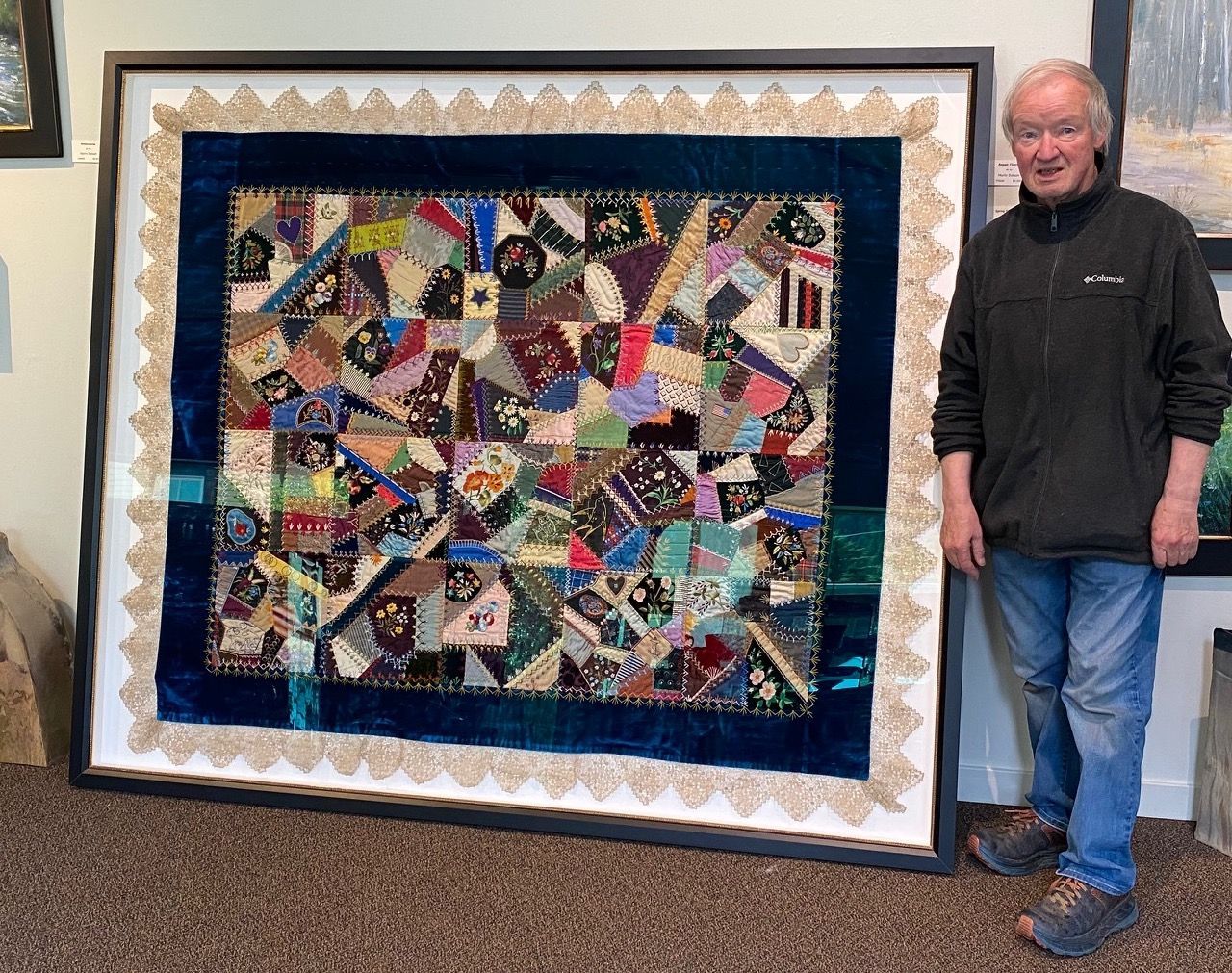 A man is standing next to a large framed quilt