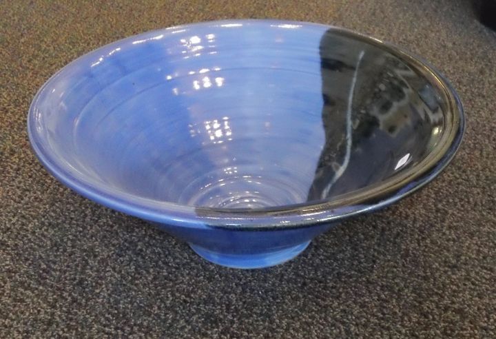 A blue bowl with a black rim is sitting on a carpet.