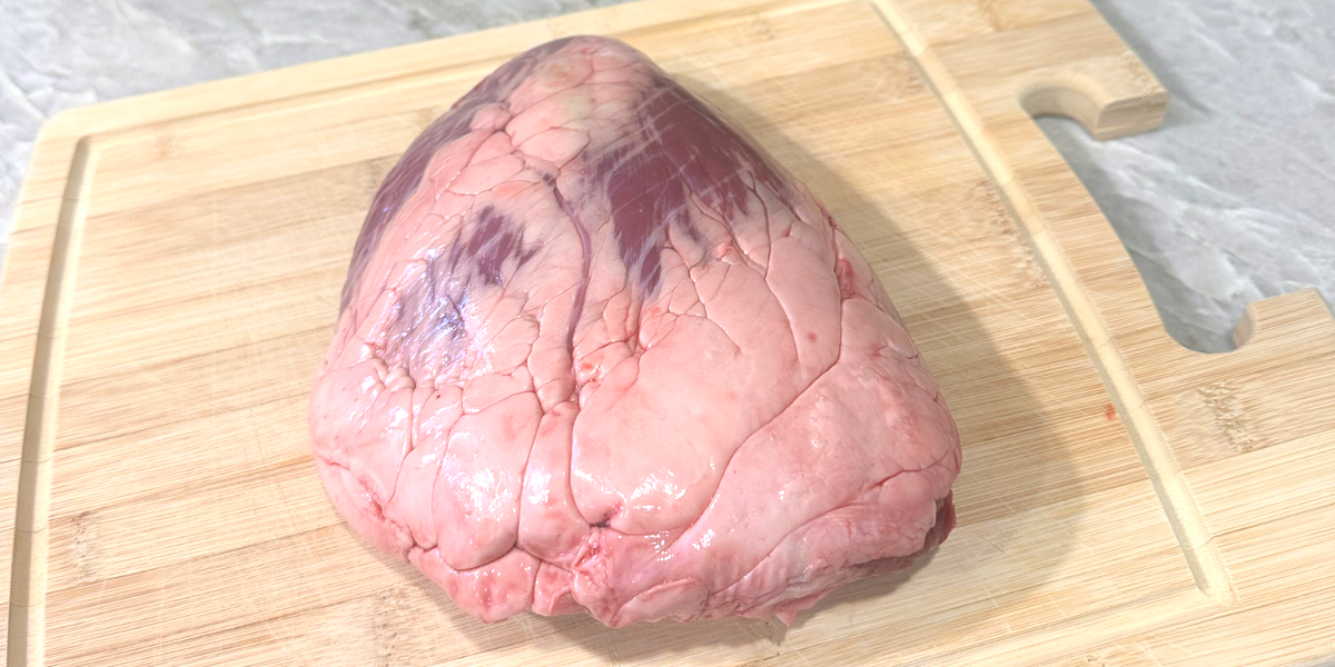 Raw beef heart meat, showing marbled muscle and fat on a cutting board