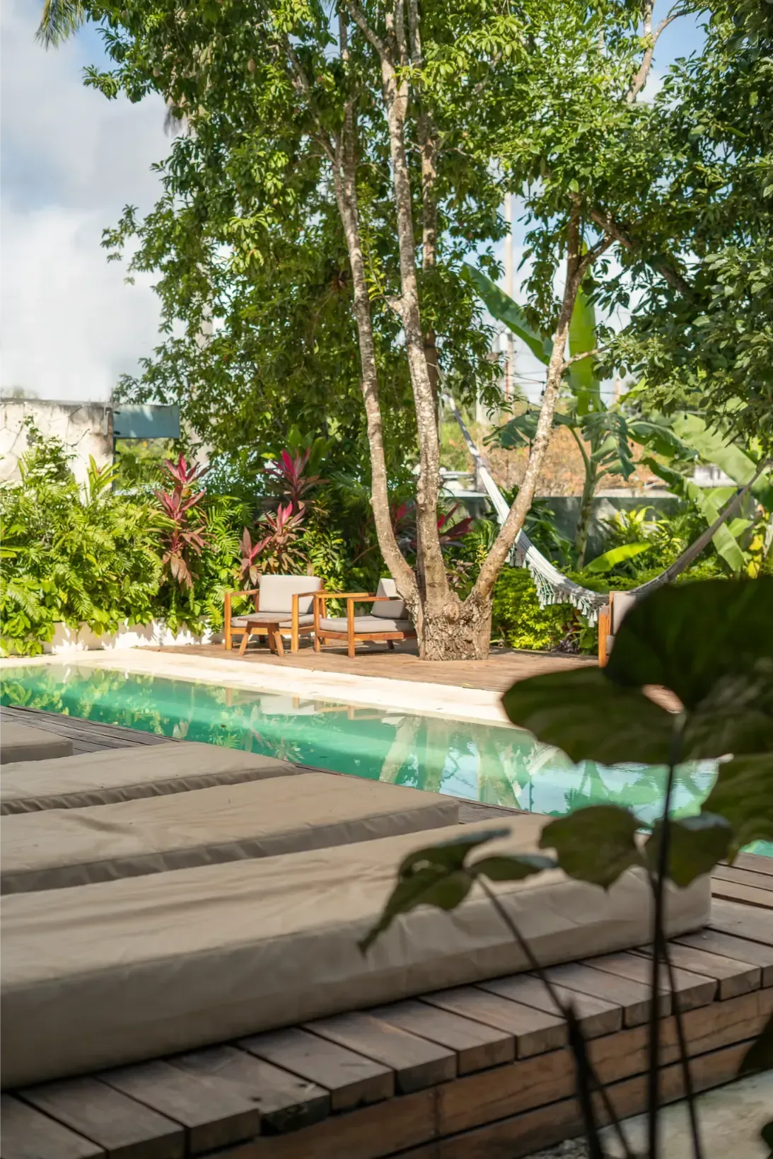 Área de relajación junto a la piscina con reposeras, terraza de madera, árboles y hamaca.