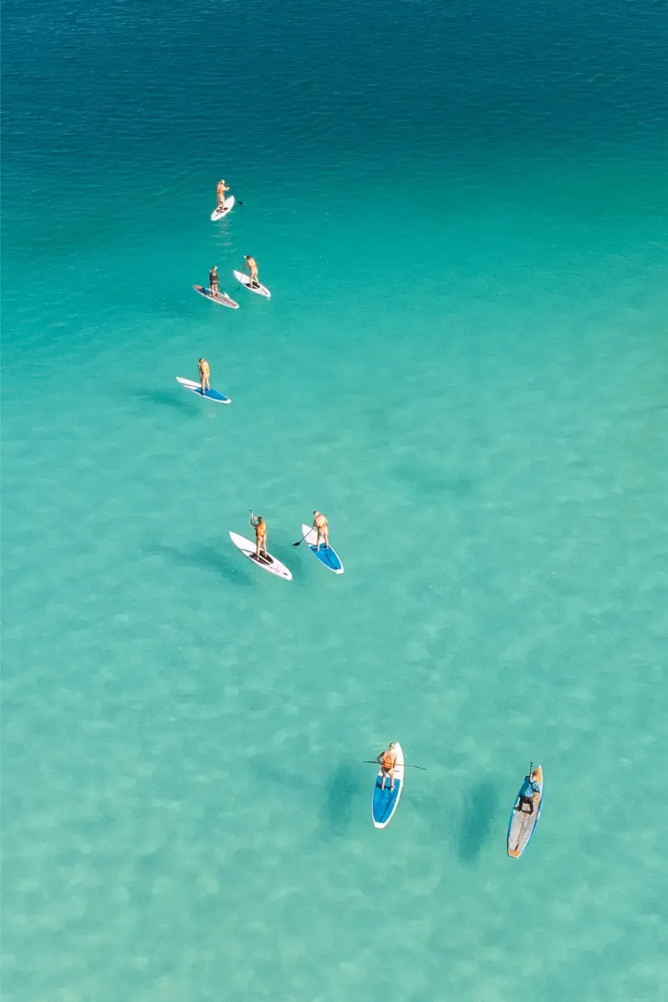 Paddleboarders en un mar turquesa, disfrutando del sol.