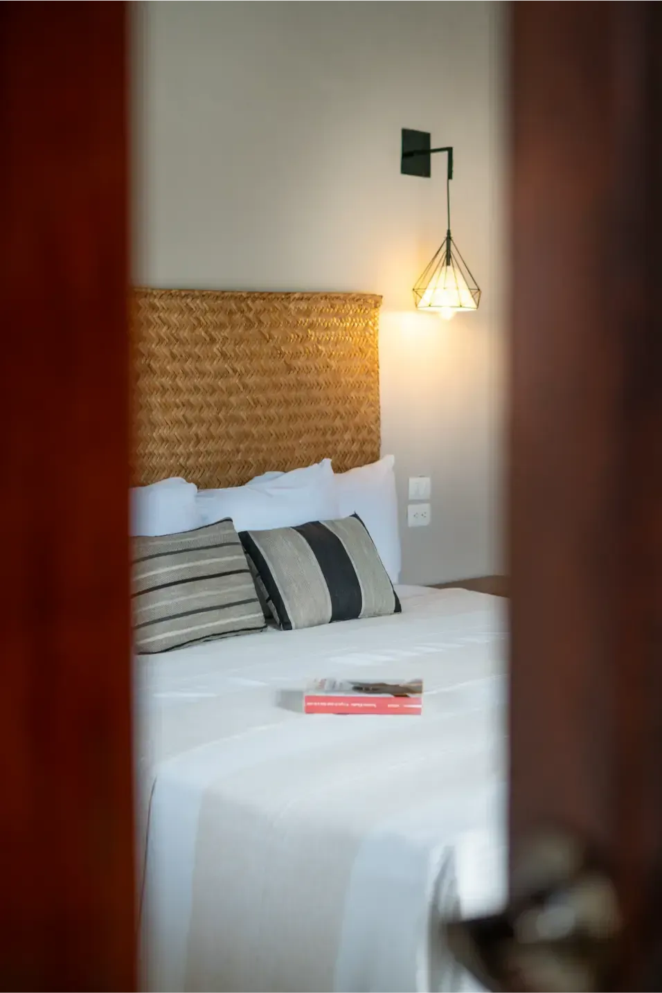 Interior de dormitorio, cama con cabecera tejida y almohadas de rayas, iluminación suave, libro sobre la cama.