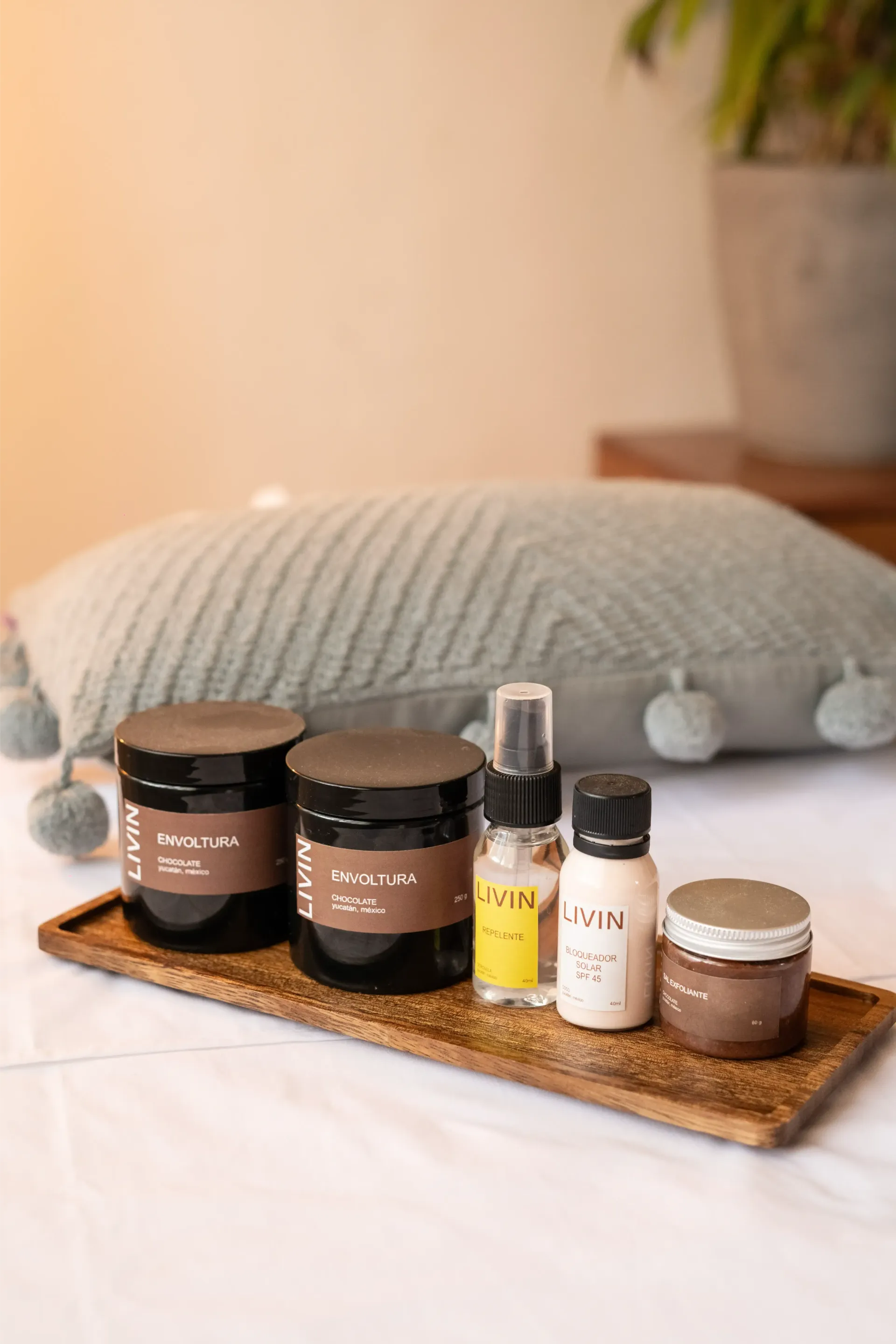 Productos para el cuidado de la piel en una bandeja de madera, colocada sobre una superficie blanca con una almohada.