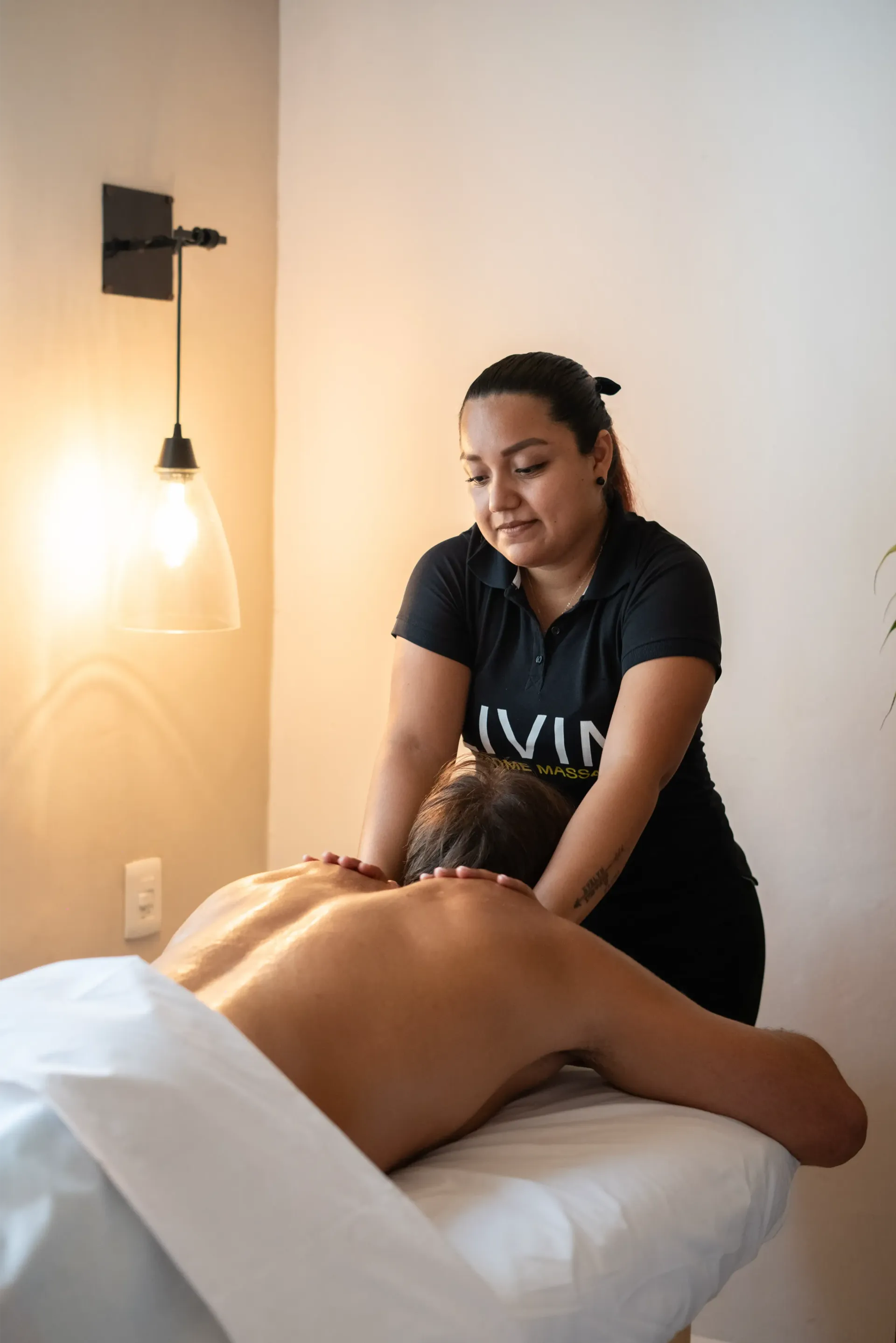 Mujer dando un masaje de espalda a una persona acostada boca abajo en una mesa de masajes en una habitación bien iluminada.