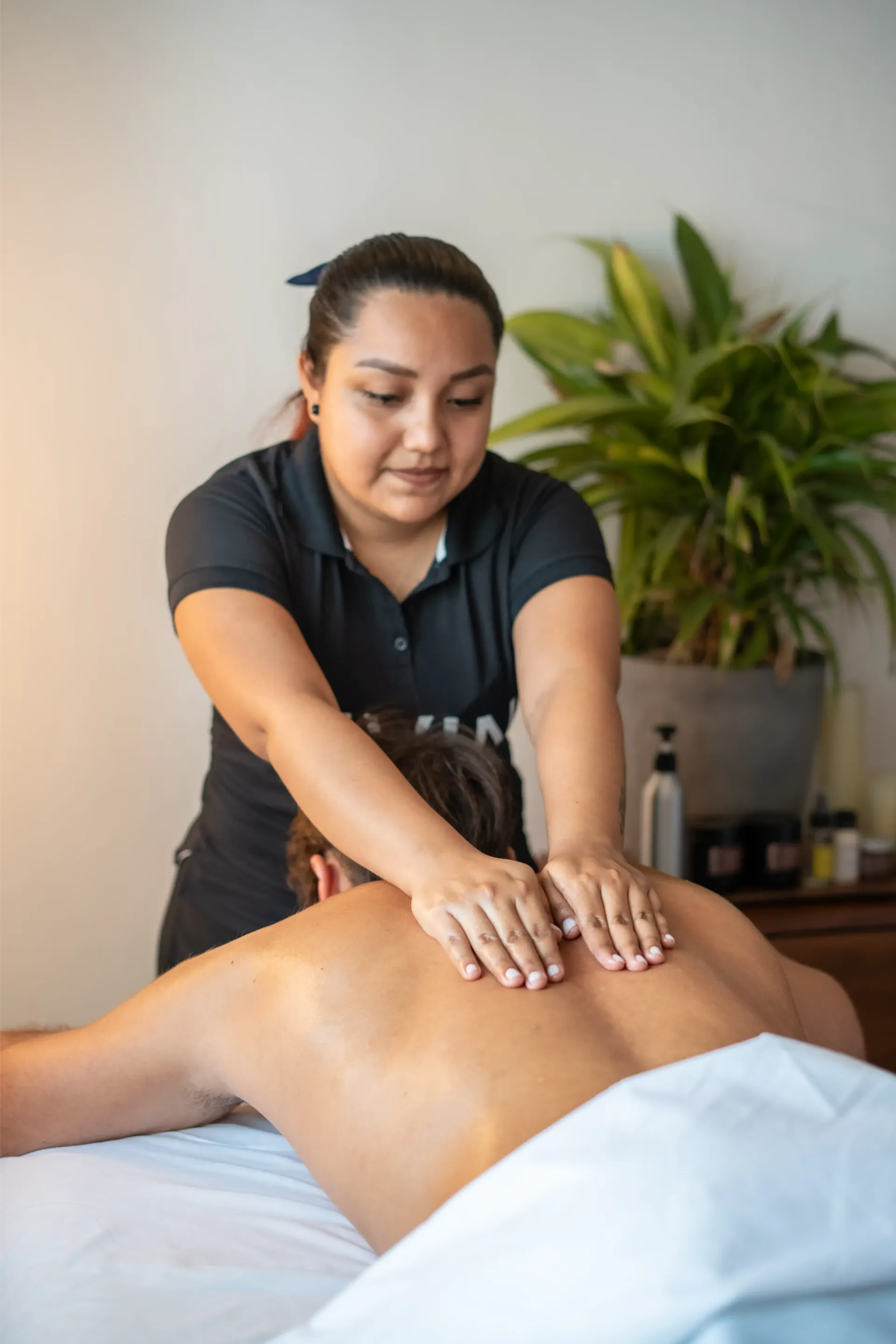 Mujer dando un masaje de espalda a una persona acostada en una mesa de masajes en una habitación bien iluminada.