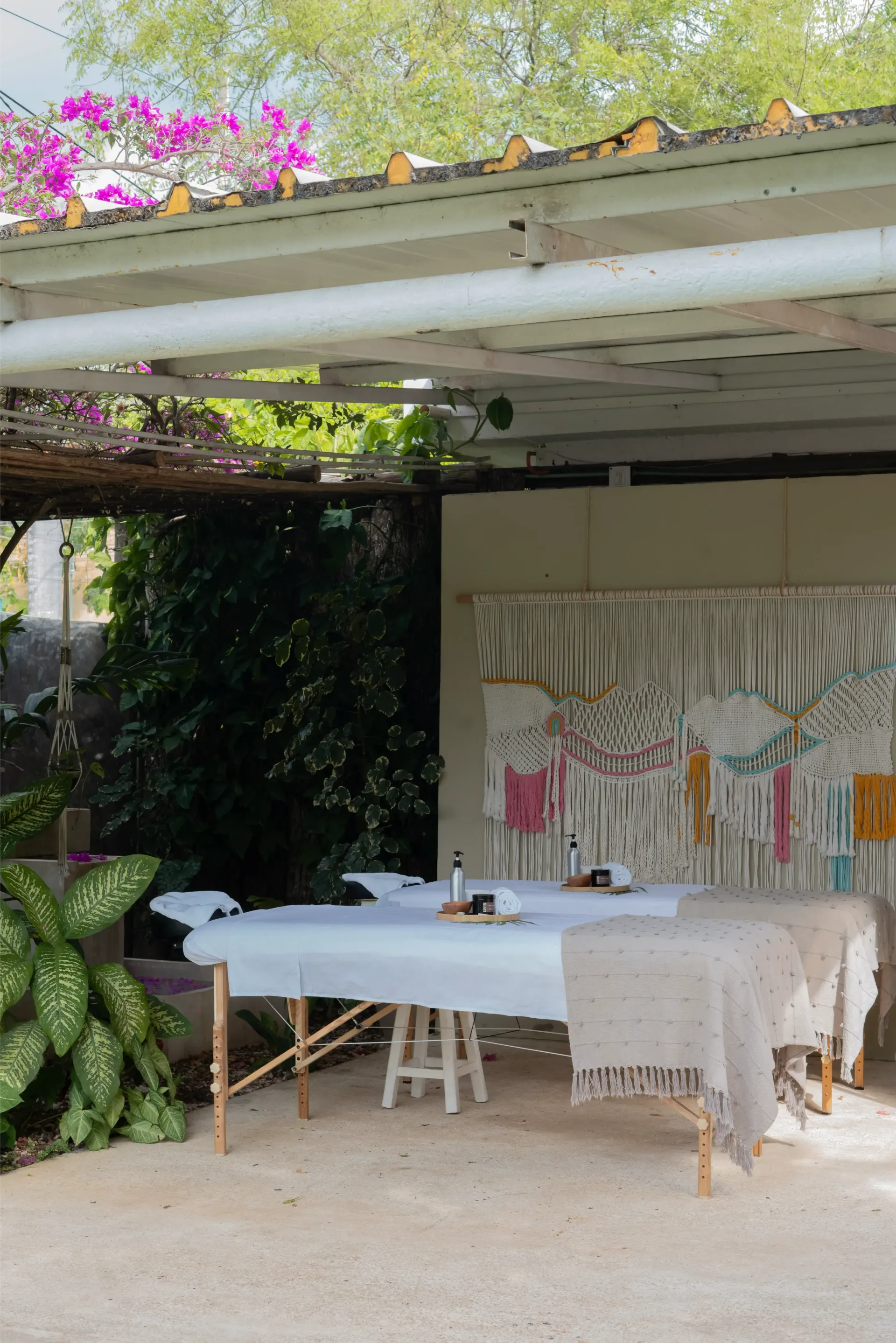 Mesa de masajes instalada al aire libre bajo una estructura de sombra, con macramé decorativo colgando al fondo.