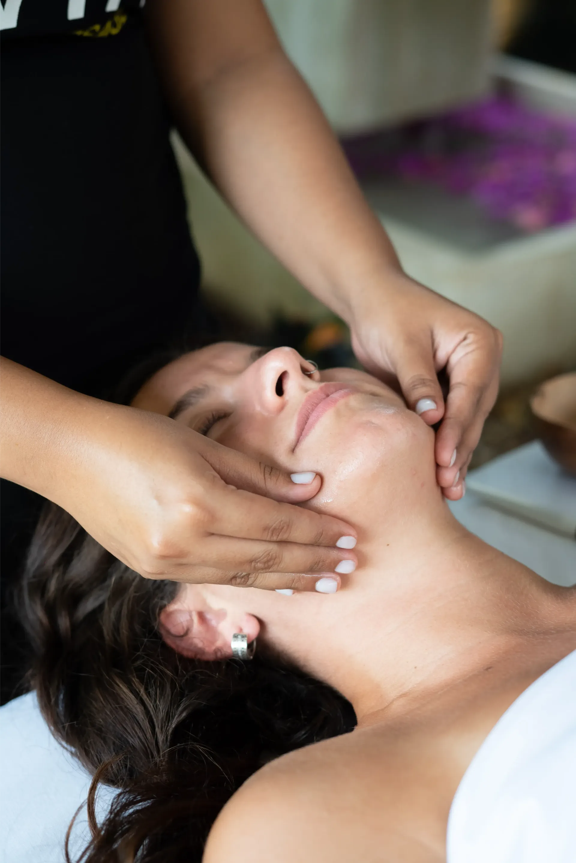 Masaje facial realizado a una mujer de cabello castaño, al aire libre cerca de flores.