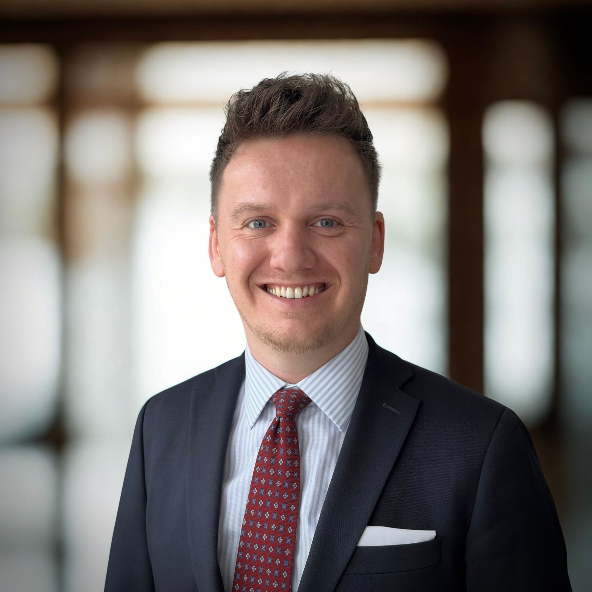 Man in pak en stropdas lacht, witte achtergrond.