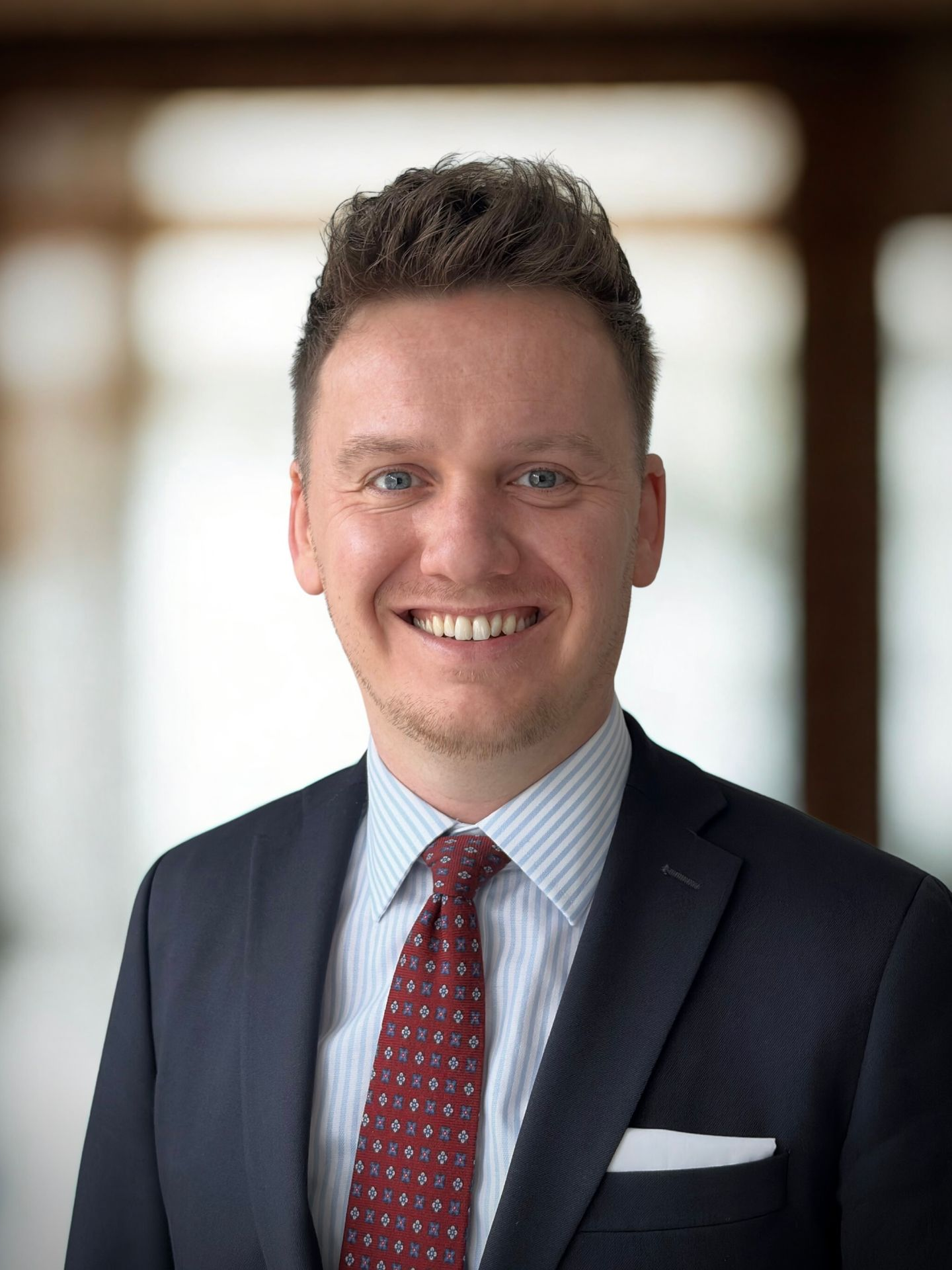 Man in pak en stropdas lacht, witte achtergrond.