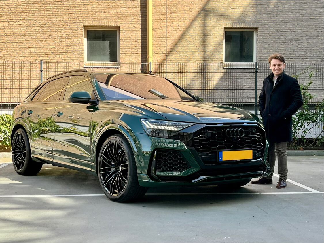 Tim van der Made naast een Audi RS Q8 op een parkeerplaats.