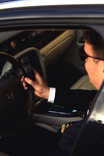 Man in pak in auto, telefoon in de hand, donker interieur.