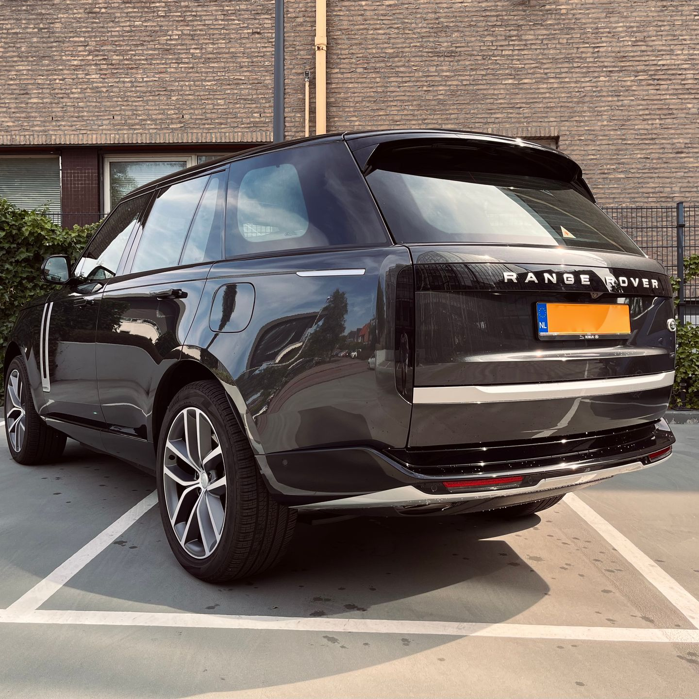 Een zwarte Range Rover staat geparkeerd op een parkeerplaats voor een bakstenen gebouw.