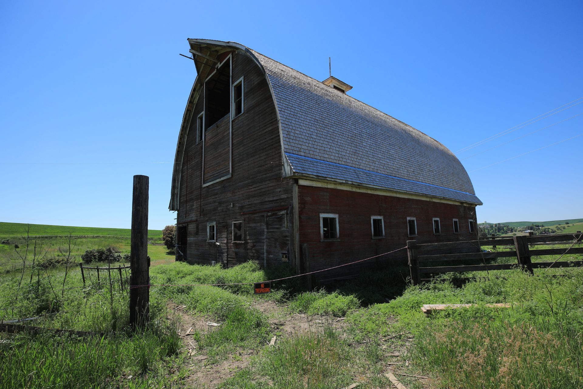 An old barn is sitting in the middle of a grassy field.