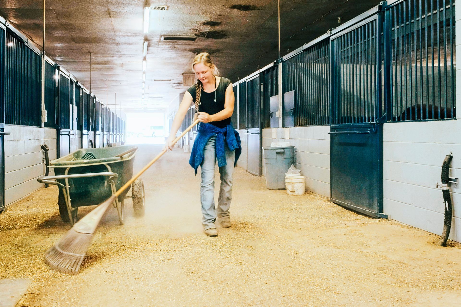A woman is sweeping the floor of a stable with a broom.