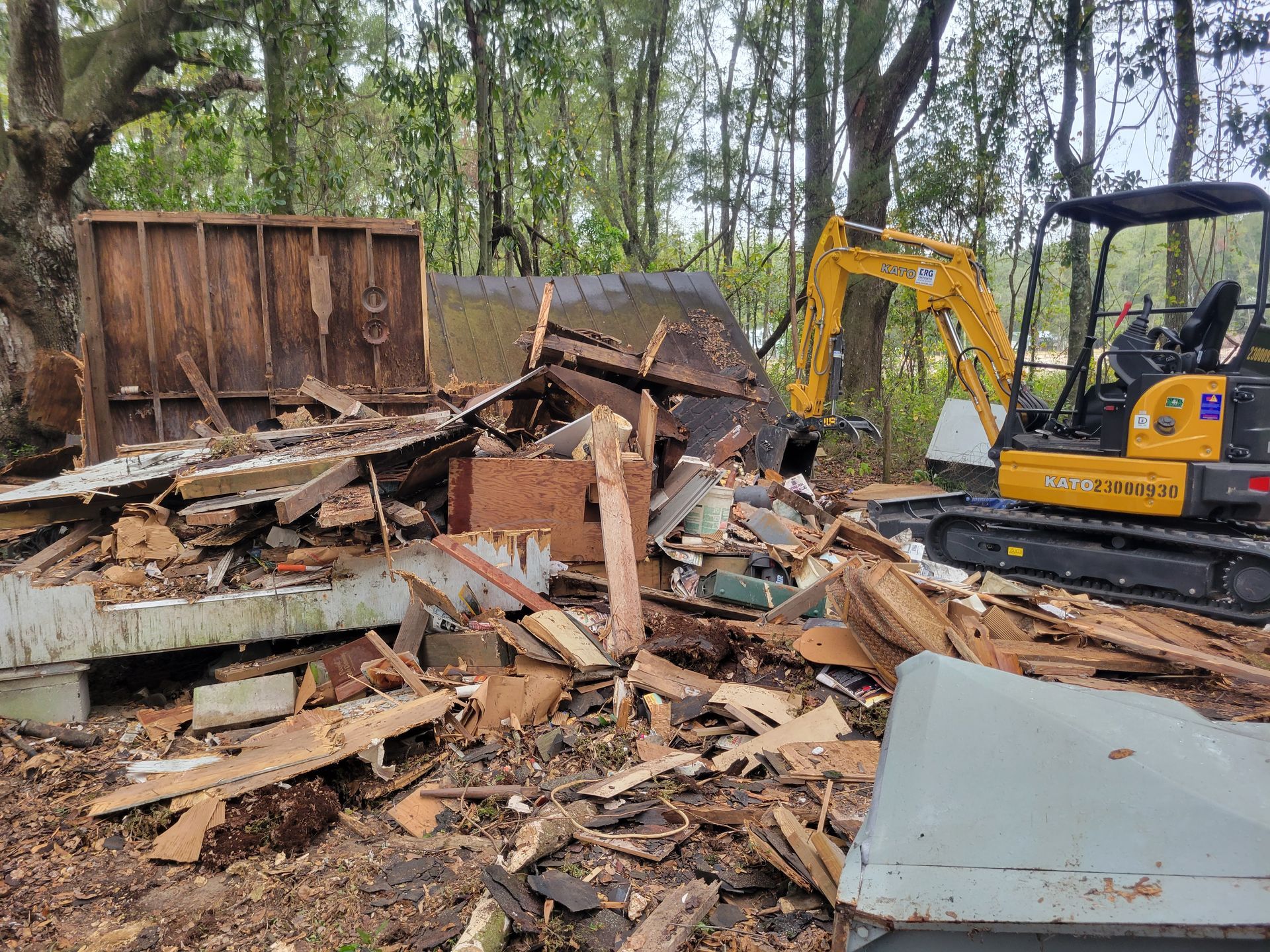 A yellow excavator is destroying a building in the woods.