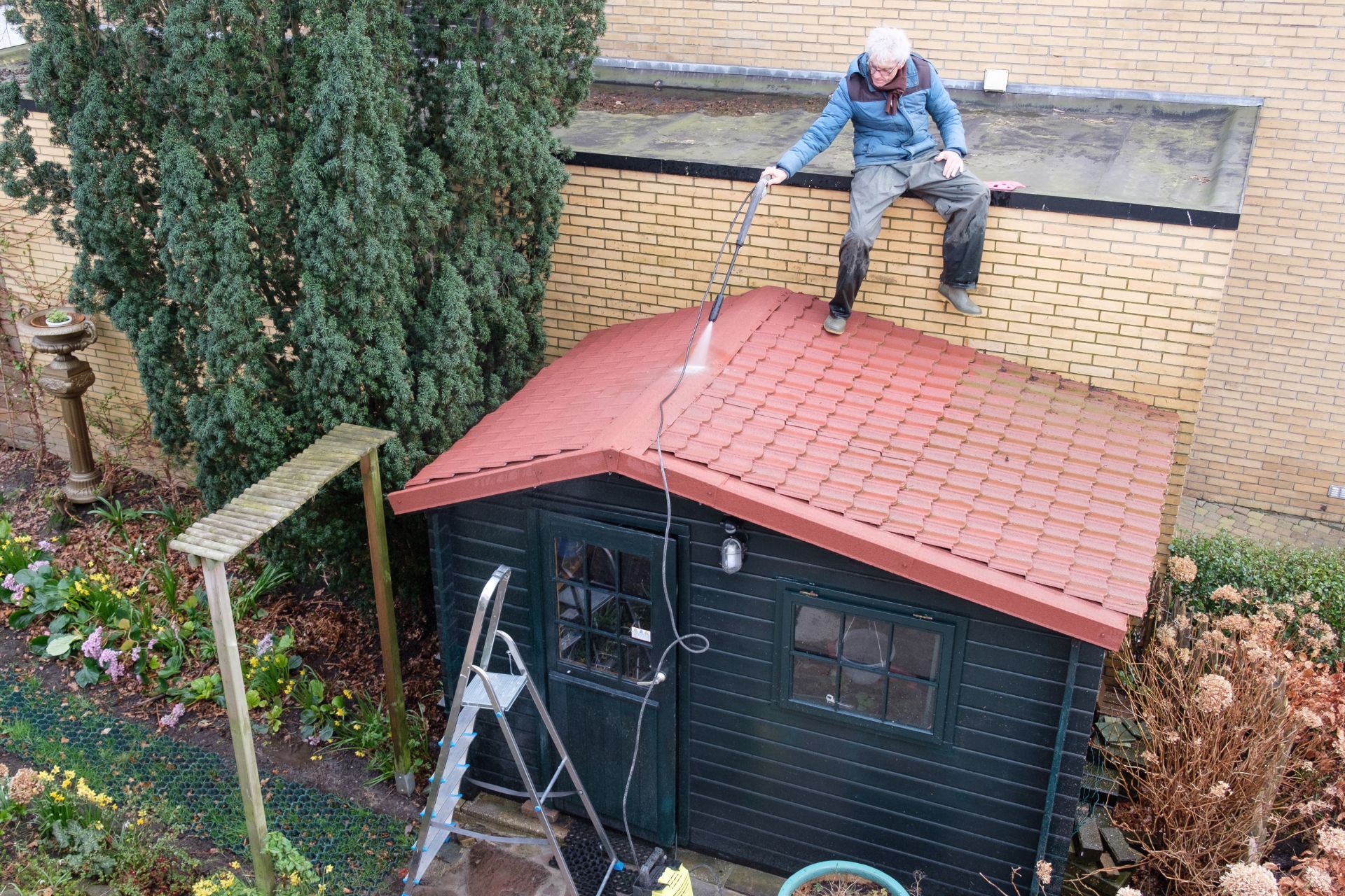 A man is cleaning the roof of a shed with a high pressure washer.