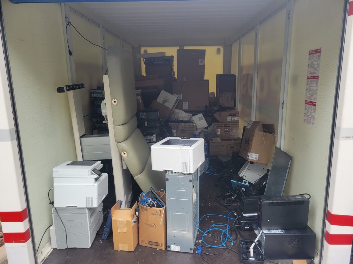 A cluttered storage unit filled with old computer equipment, boxes, and wires.
