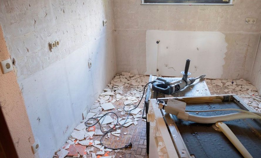 A room with a lot of broken tiles and a drill on the floor.