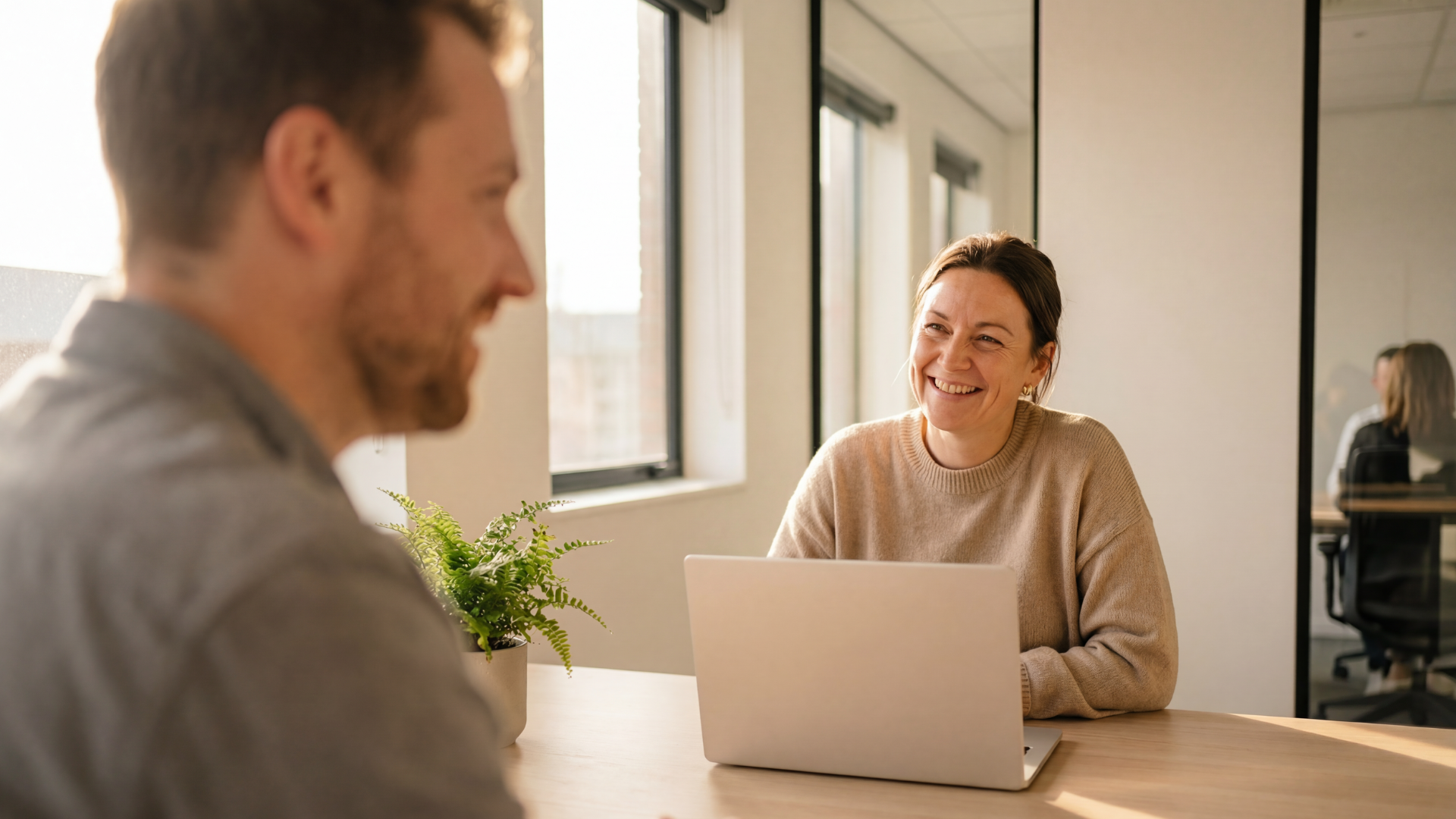 Four coworkers in an office setting. They are smiling and talking around a desk.