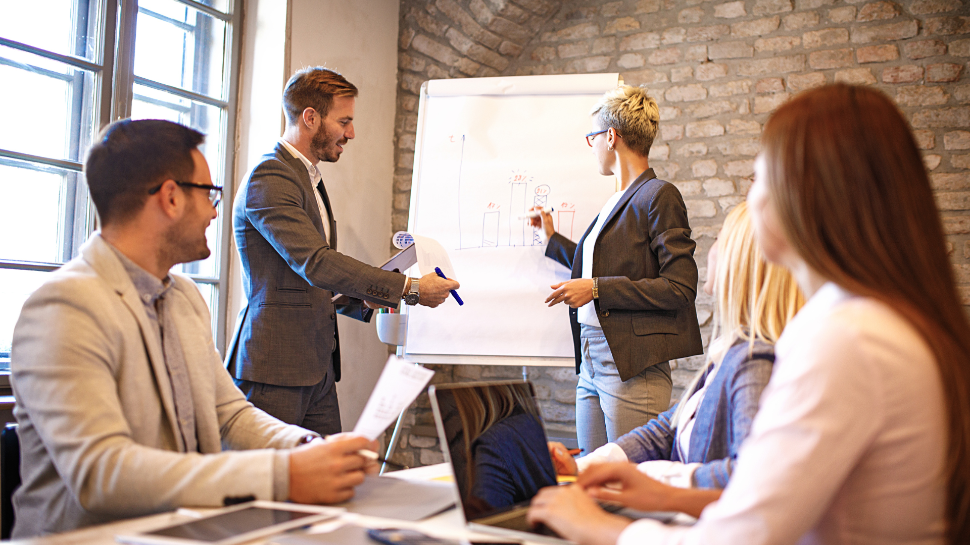 Business meeting: Woman presenting data on whiteboard, others seated, discussing and looking on.