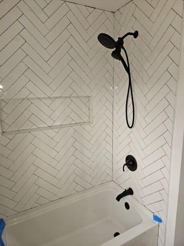 A bathroom with white tiles and a black shower head.