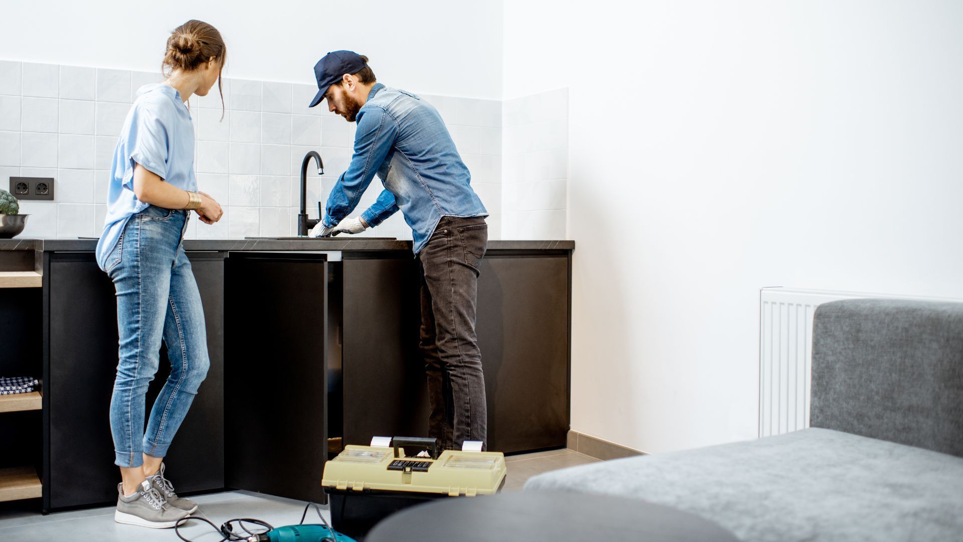 A man and a woman are working on a kitchen sink.