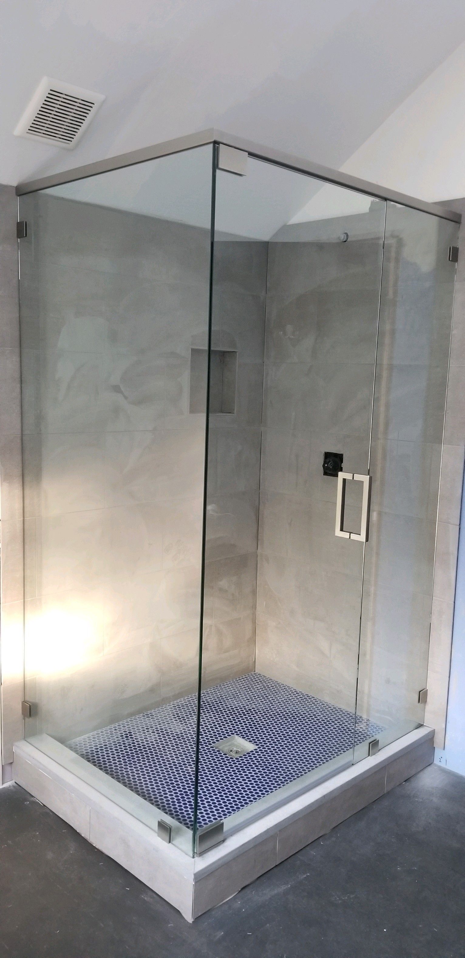 A shower stall with a glass door and a mosaic floor in a bathroom.