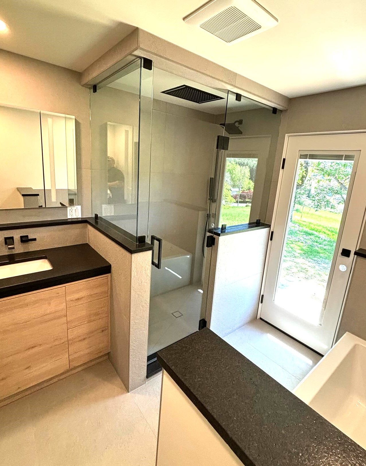 A bathroom with a walk in shower , sink , mirror and tub.
