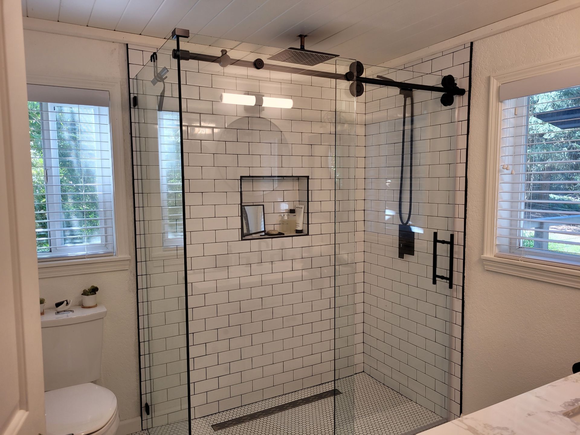 A bathroom with a glass shower door with a black handle.
