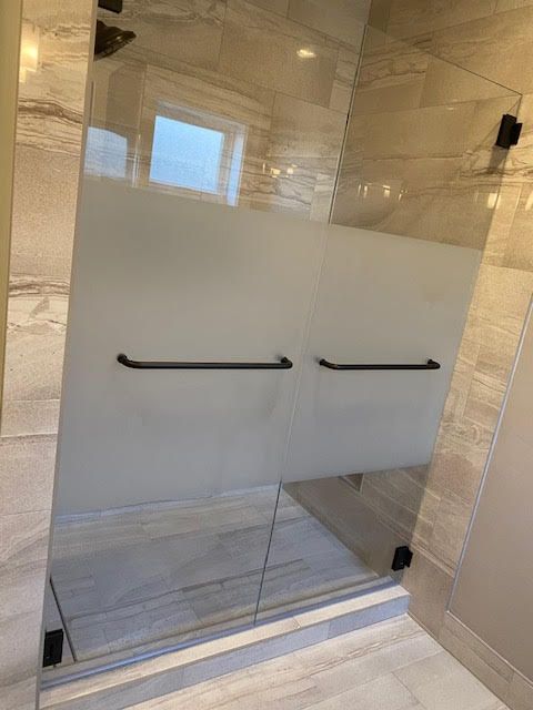 A bathroom with a glass shower door with a black handle.