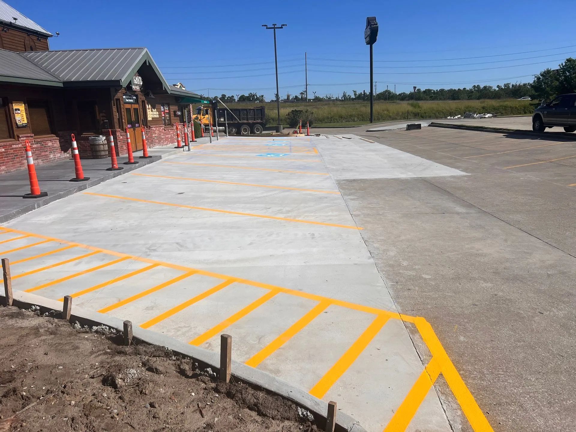 Newly paved concrete with yellow markings; cones and a ramp near a building.