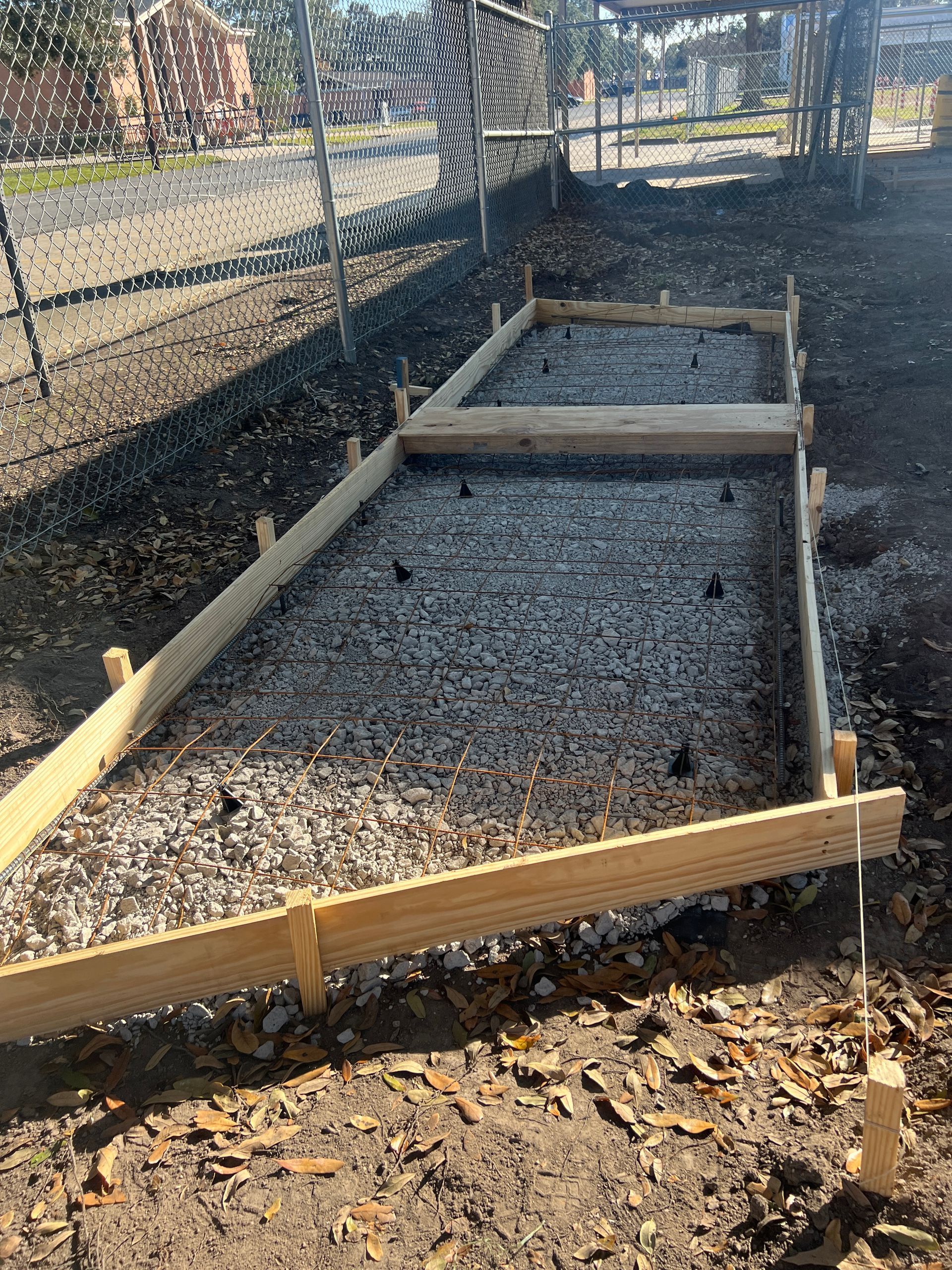 Wooden formwork outlines a gravel-filled rectangular area, prepared for concrete pouring in an outdoor setting.