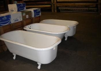 Three white bathtubs are sitting next to each other in a warehouse.