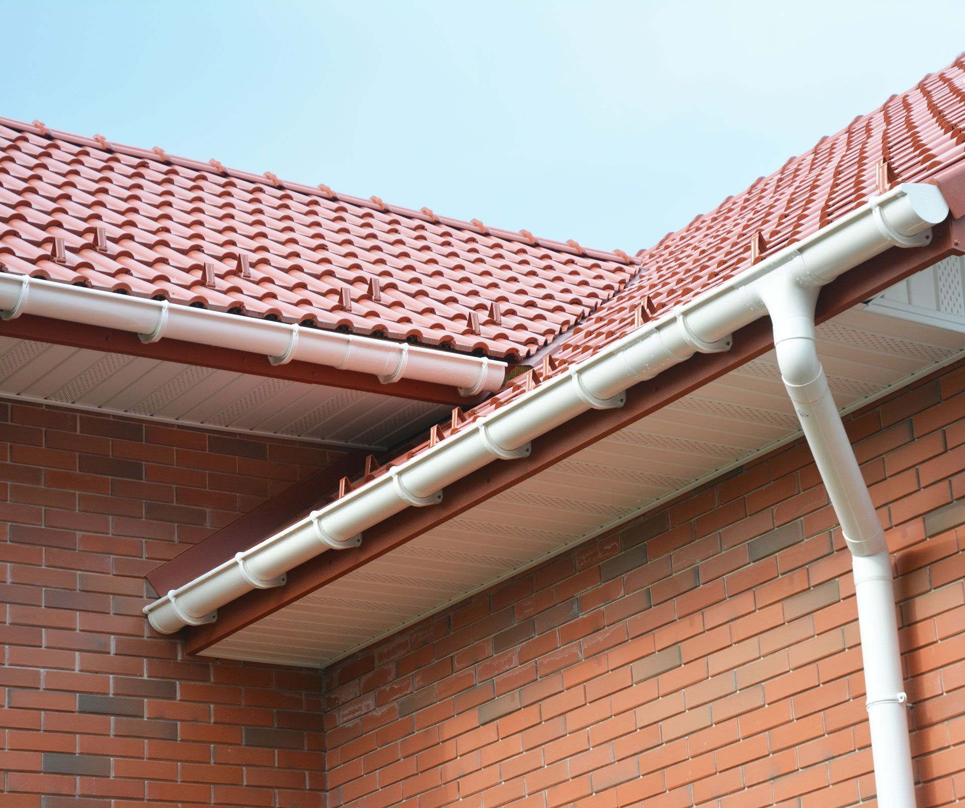 White gutters on a brick building with a red tile roof, against a blue sky.