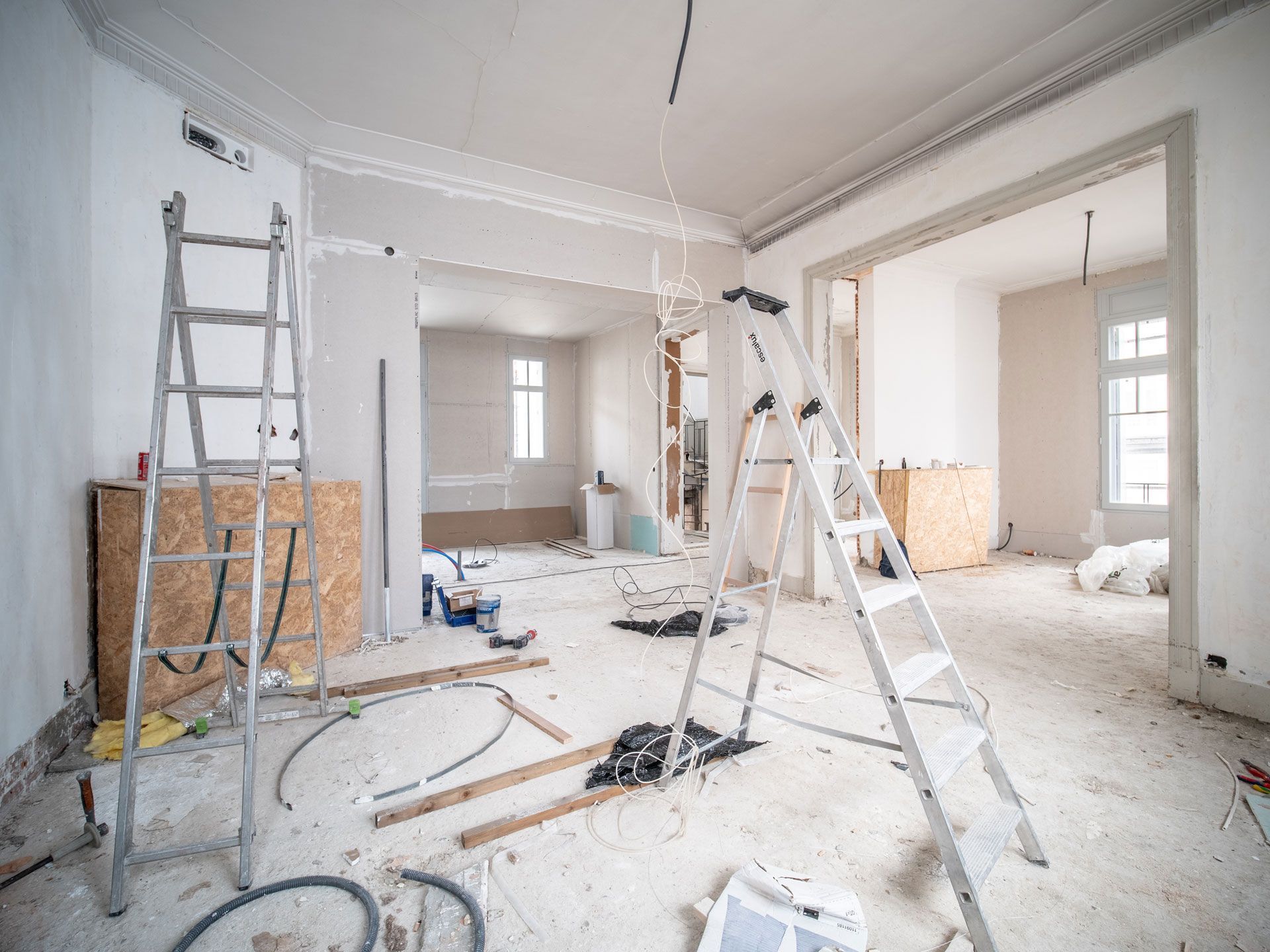 Room under renovation with ladders, debris, and exposed construction elements.