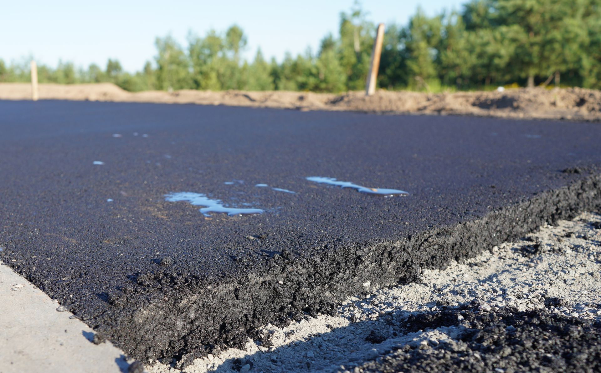 Freshly laid black asphalt on a road construction site, showing the textured edge against a gravel base.