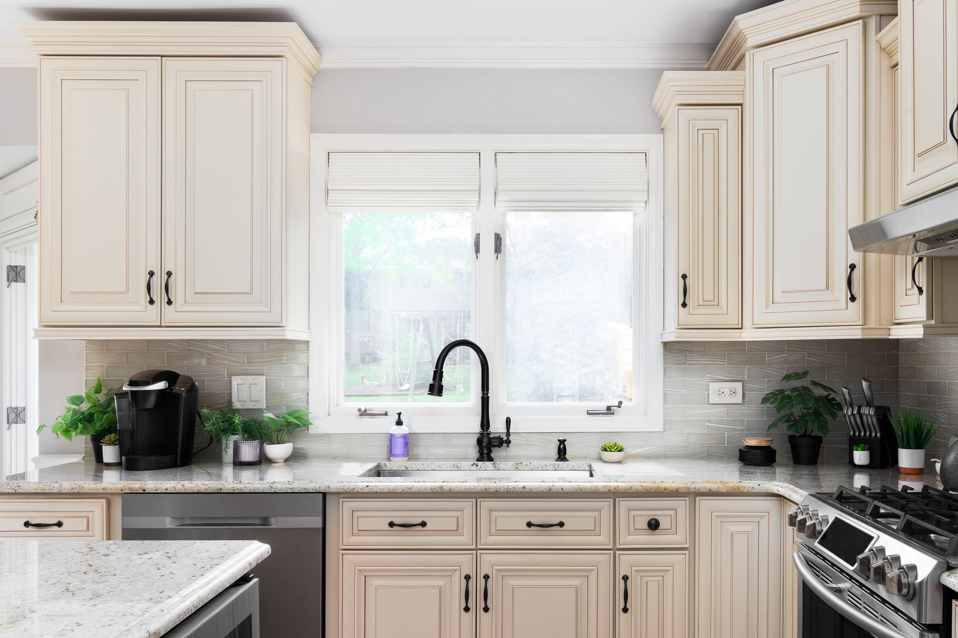 Cream-colored kitchen with cabinets, stainless steel appliances, and a window over the sink.